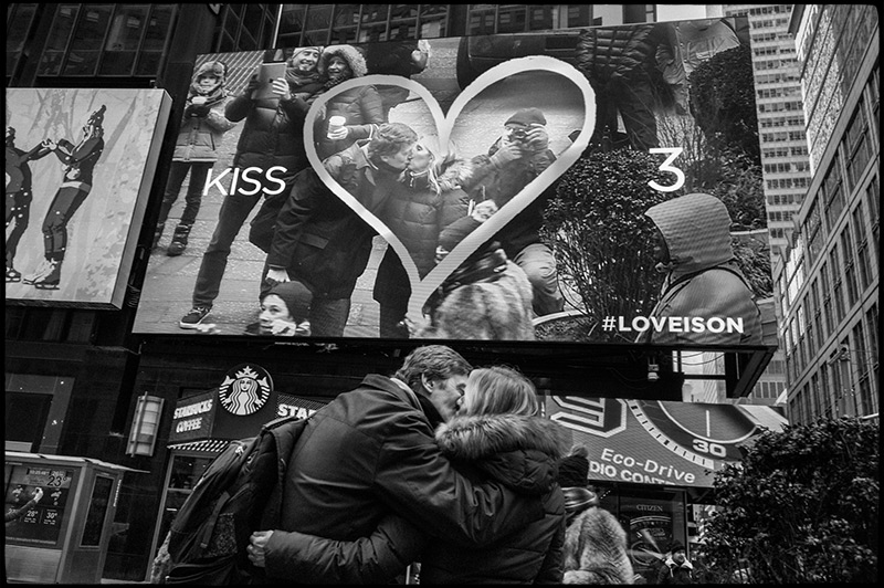 Black and white photograph of advertising billboards including live video feed in Times Square.