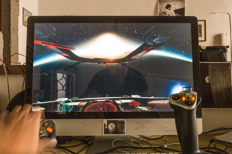 Elite on an iMac with my blurred hand over the throttle of a Saitek HOTAS.